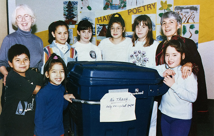 Color photograph of the Earthsavers Club from the 1996 Forest Edge yearbook. Seven students and two sponsors are standing around a large, blue recycling bin. A sign on the bin reads: No Trash! Only recycled paper.